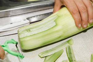 recept voor courgette beignets. stap 1 - de courgette schillen. handen schillen groene courgette foto