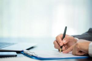 werkplaats detailopname persoon professioneel zakenvrouw zittend Bij bureau houden pen ondertekening of handtekening contract papier. werknemer vrouw schrijven overeenkomst document Aan papierwerk het formulier zakelijke Bij werk kantoor foto