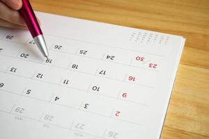kalenderpagina met vrouwelijke hand met pen op bureautafel foto