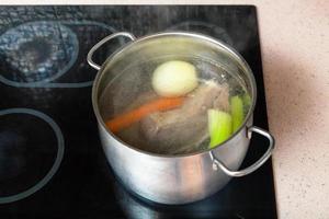 voorbereidingen treffen vlees bouillon in soeppan Aan keramisch kookplaat foto