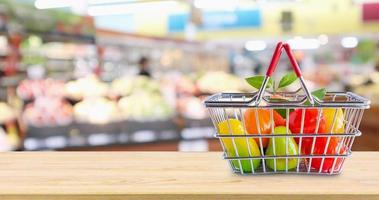 winkelmandje met fruit op houten tafel over supermarkt supermarkt wazige achtergrond foto