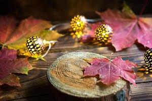 herfst nog steeds leven van gedaald esdoorn- rood en geel bladeren en warm lichten slingers Aan een houten achtergrond. focus Aan een blad Aan een sectie van een boom. de atmosfeer van de vakantie, halloween, dankzegging. foto