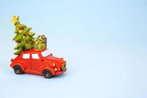Kerstmis decor - een rood retro auto draagt een Kerstmis boom met geschenk dozen Aan de dak. speelgoed- met pailletten Aan een blauw achtergrond, ruimte voor tekst. nieuw jaar foto