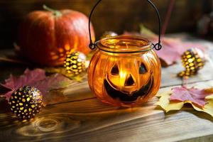 lamp pompoen met ogen en mond gemaakt van glas en natuurlijk oranje pompoen Aan een houten tafel met geel en rood esdoorn- bladeren. halloween, warm herfst atmosfeer. ronde guirlande, kaars in een kandelaar. foto