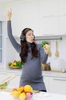 mooi, koel, zwanger vrouw gelukkig Koken biologisch en gezond salades in haar modern keuken. nieuw mam toepassingen broccoli in plaats daarvan van microfoon naar zingen en Speel voor plezier. mooi zo humeur concept foto