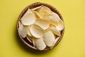 aardappel chips tussendoortje Aan mand, krokant aardappel chips Aan de keuken tafel geel achtergrond foto