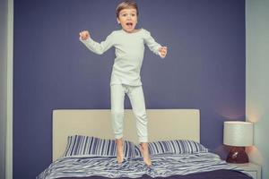 opgewonden jongen jumping Aan de bed. foto