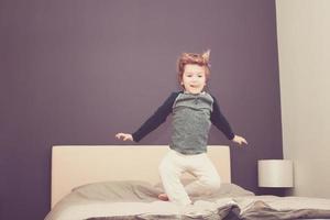 speels kind jumping Aan de bed. foto