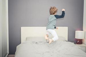 speels jongen hebben pret terwijl jumping Aan de bed. foto