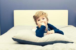 portret van schattig weinig jongen aan het liegen naar beneden Aan de bed. foto