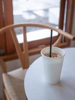 ijs melk koffie in wit duidelijk leeg papier kop Aan tafel in de buurt glas venster in minimaal Japans stijl cafe foto