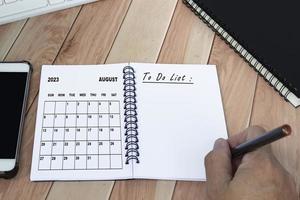 handen met pen schrijven naar Doen lijst met augustus 2023 kalender Aan notebook. foto