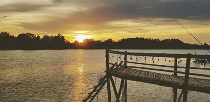 silhouet van houten waterkant, waterkant of brug met rive en boom achtergrond Bij zonsondergang of zonneschijn tijd. mooi natuur en vrijheid concept. natuurlijk behang met kopiëren ruimte in wijnoogst toon. foto