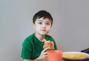 kind jongen croissant voor zijn ontbijt voordat Gaan naar school- in de ochtend, gezond voedsel voor kind concept foto