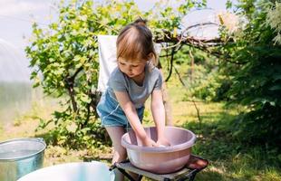 klein kleutermeisje helpt met de was. kind wast kleren in de tuin foto