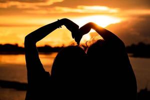 silhouet vrouw maken hartvormig handen met zonsopkomst in de buurt de vorm en meer achtergrond, liefde concept. gelukkig Valentijnsdag dag foto