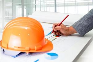 aziatische ingenieur met architectonisch huisplan projectblauwdruk, grafiek en gele helm en technische constructiehulpmiddelen. foto