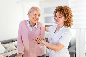 glimlachen verpleegster helpen senior dame naar wandelen in de omgeving van de verpleging huis. portret van gelukkig vrouw verzorger en senior vrouw wandelen samen Bij huis. professioneel verzorger nemen zorg van ouderen vrouw. foto