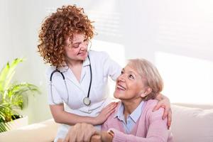 dichtbij positief verhouding tussen senior geduldig en verzorger. gelukkig senior vrouw pratend naar een vriendelijk verzorger. jong mooi verzorger en ouder gelukkig vrouw foto