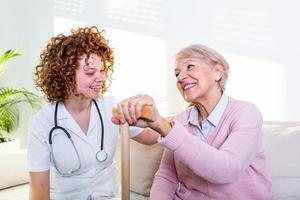 jong verzorger en senior vrouw lachend samen terwijl zittend Aan bank. senior vrouw en jonger vriend hebben pret samen gedurende vergadering Bij huis. foto