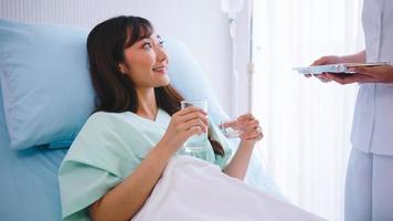 vrouw verpleegster geven geneeskunde naar Aziatisch vrouw aan het liegen Aan bed na chirurgie. foto