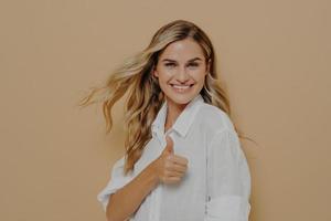 opgewonden mooie blonde vrouw poseren in studio met duim omhoog ok teken foto