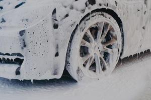 autowiel in wit zeepschuim bij carwash-servicestation foto