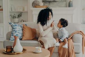 portret van liefhebbende Afro-Amerikaanse zwangere moeder die zoontje uitlegt over haar zwangerschap foto