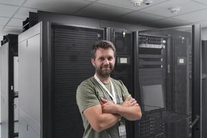 portret van mannetje technicus of netwerk beheerder staand dapper net zo een held met armen gekruiste in gegevens centrum server kamer. foto