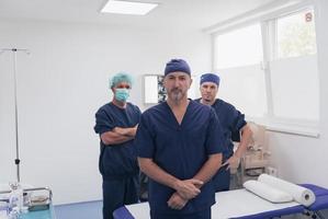 multi-etnisch orthopedische dokter in voorkant van zijn medisch team op zoek Bij camera vervelend gezicht masker foto