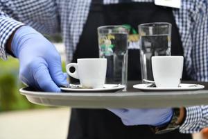 ober in een medisch beschermend masker serveert de koffie in restaurant foto