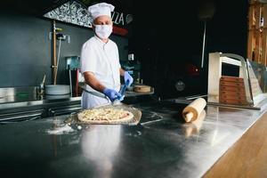 chef met beschermend coronavirus gezicht masker voorbereidingen treffen pizza foto