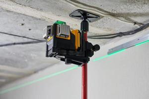 laserniveaumeetinstrument met zichtbare groene laserstraal op muur voor installatie van spanplafond foto