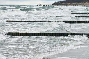 uitzicht op blauwe zee met schuimende golven en houten golfbrekers foto