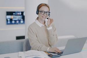 online tolk. jonge gelukkige vrouw in hoofdtelefoon praat met de klant voor de laptop. foto