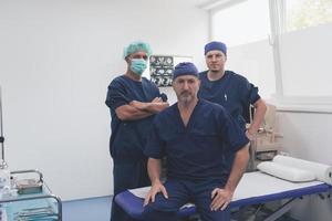 multi-etnisch orthopedische dokter in voorkant van zijn medisch team op zoek Bij camera vervelend gezicht masker foto