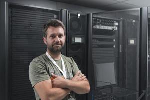 portret van mannetje technicus of netwerk beheerder staand dapper net zo een held met armen gekruiste in gegevens centrum server kamer. foto