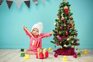 weinig baby Open de geschenk doos met decoreren Kerstmis boom Aan groen achtergrond foto