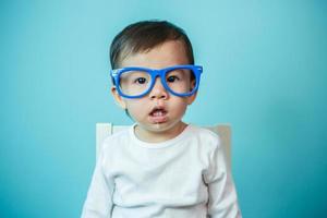 schattig Aziatisch baby lachend vervelend bril Aan blauw achtergrond, studio schot foto