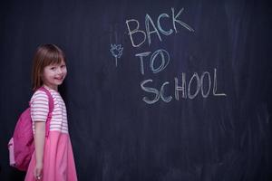 school- meisje kind met rugzak schrijven schoolbord foto