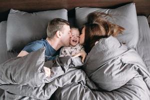 gelukkig kind met ouders in bed Bij huis foto