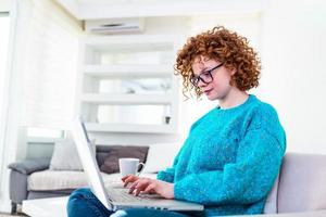 positief jong vrouw freelancer aan het kijken video in blog Aan netbook en hebben een koffie Bij comfortabel huis. mooi jong bedrijf vrouw werken Aan laptop.freelancer Verbinden naar internet foto