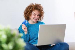 jong vrouw Holding credit kaart en gebruik makend van laptop computer. online boodschappen doen concept. gelukkig vrouw aan het doen online boodschappen doen Bij huis foto