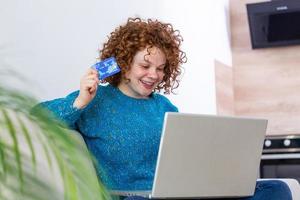 schattig rood haar- vrouw boodschappen doen online met credit kaart. vrouw Holding credit kaart en gebruik makend van laptop. online boodschappen doen concept foto