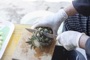 de hand- van de straat verkoper draag- een mes, besnoeiing uit de ananas kurk. foto