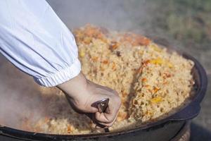 koken kookt pilaf in een ketel. pilaf met groenten en vlees gekookt over- een Open brand. foto