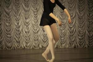 danser Aan fase. meisje in een zwart jurk en beige panty, voorkant visie. foto