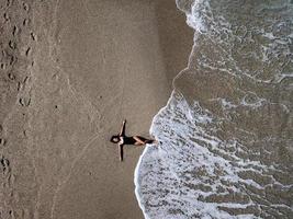 antenne top visie jong vrouw aan het liegen Aan de zand strand en golven foto