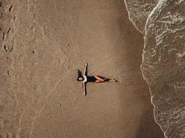 antenne top visie jong vrouw aan het liegen Aan de zand strand en golven foto