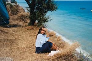 aantrekkelijk vrouw in zomer rok en overhemd zit Aan de kust foto